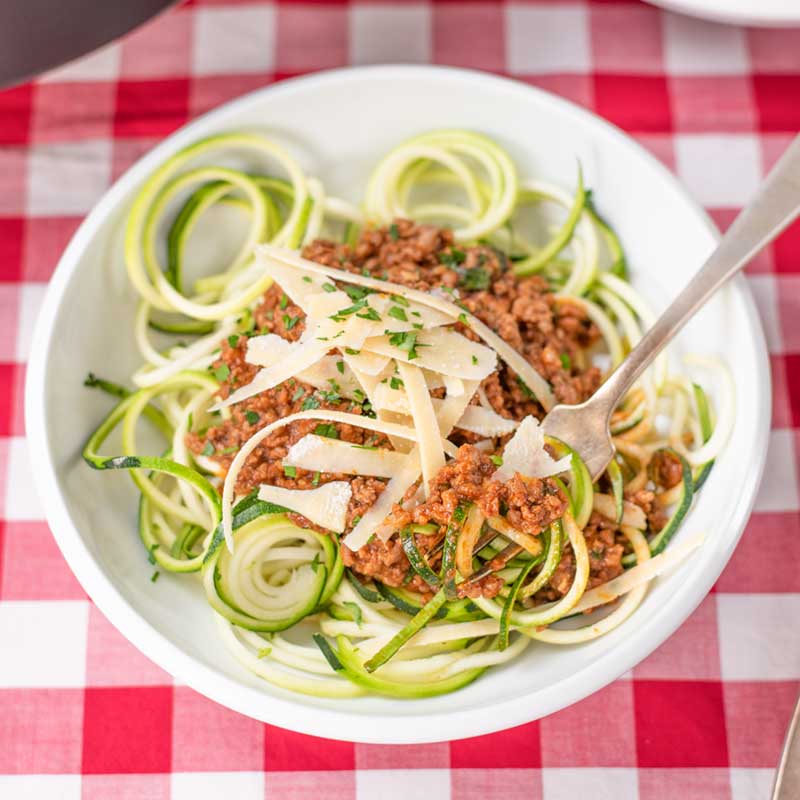 Keto Bolognese Sauce in a bowl with zucchini noodles and parmesan cheese on a red checked table