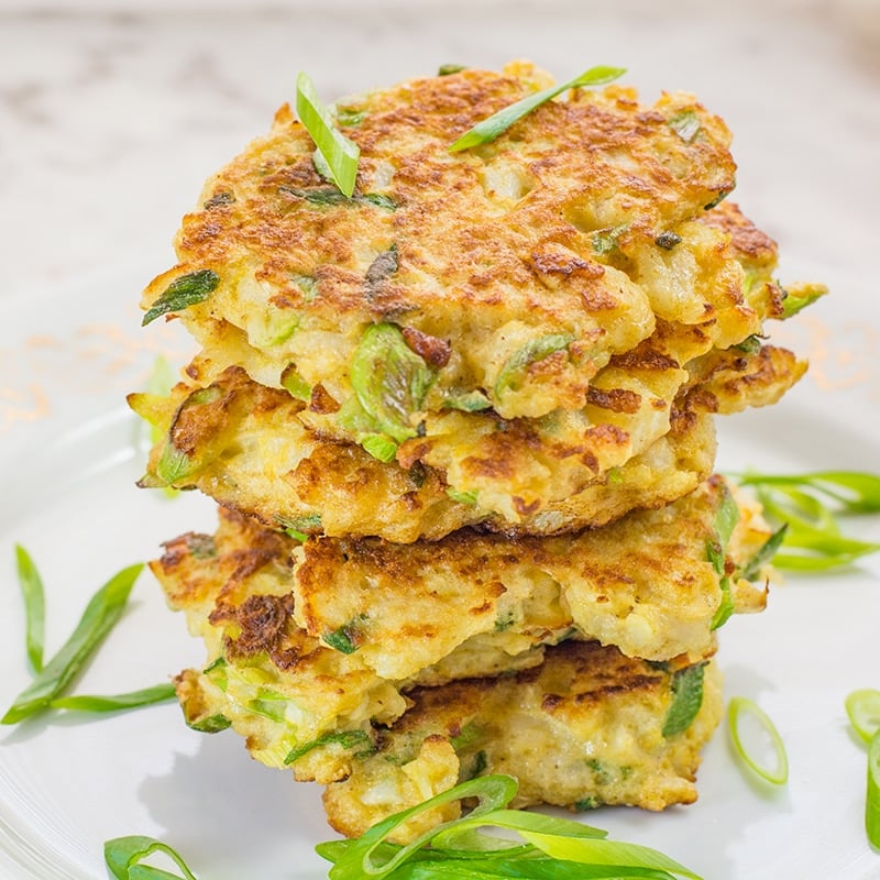 Low Carb Cauliflower Fritters stacked on a plate and topped with scallions