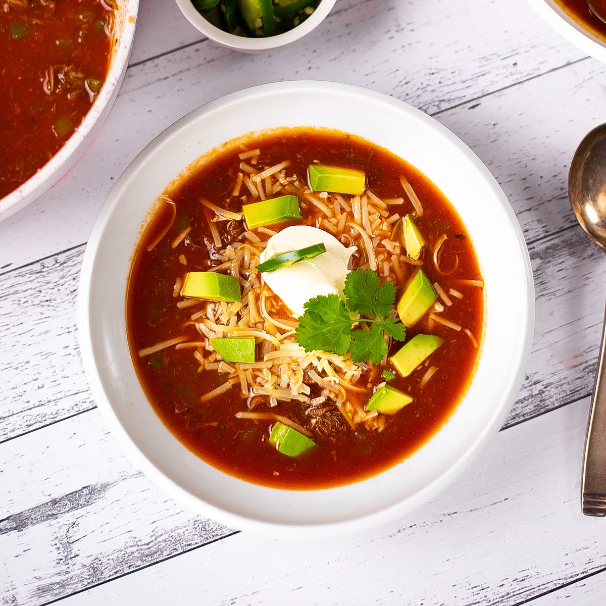 Keto taco soup in a white soup bowl with a spoon to te side on a table.