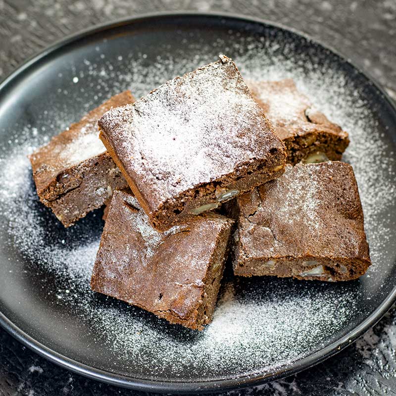 Keto Chocolate Macadamia Brownies on a plate covered with icing sweetener