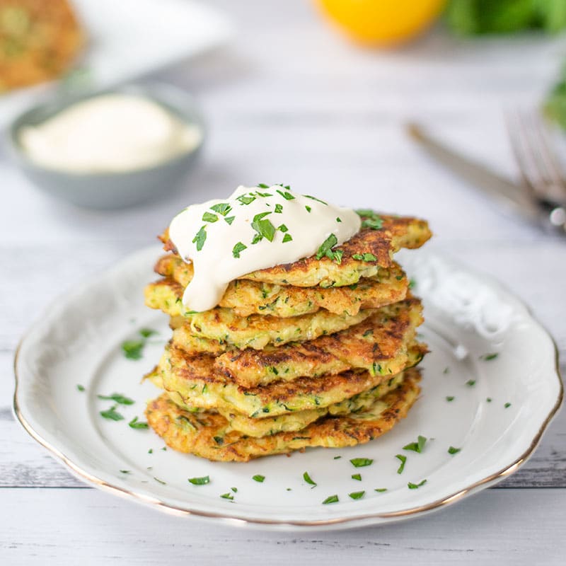 Keto Zucchini Fritters stacked on a plate and topped with sour cream