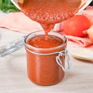 Keto Enchilada Sauce being poured from a saucepan into a glass jar