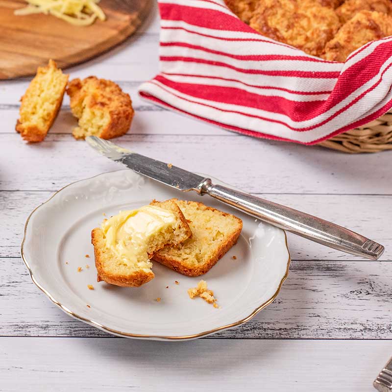 Keto Three Cheese Biscuits przekrojone na pół na białym talerzu z masłem