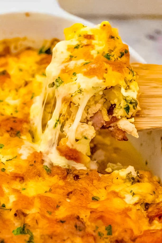 Keto chicken, cheese, and bacon casserole in a white baking dish being scooped up with a spoon.