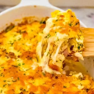 Keto chicken, cheese and bacon casserole in a white baking dish being scoop up with a wood spoon.