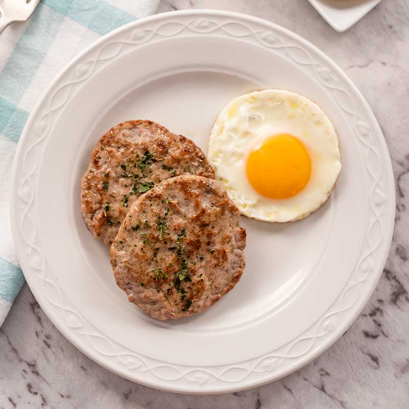 Image shows two keto breakfast sausage patties with a fried egg on a white plate