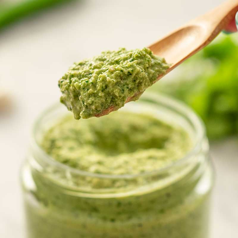 Image show a wooden scoop filled with low carb thai green curry paste, the jar of curry paste is in the background