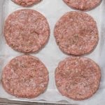 Image shows 4 raw keto breakfast sausage patties on a lined cookie sheet