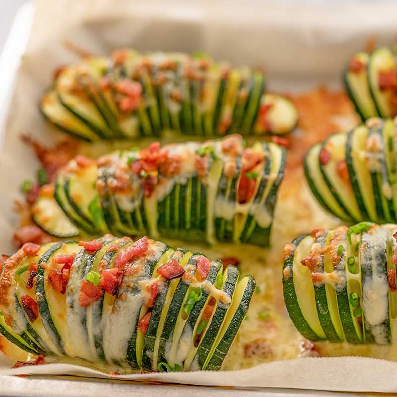 Image of 6 pieces of keto hasselback zucchini stuffed with cheese and bacon sitting on a cookie sheet