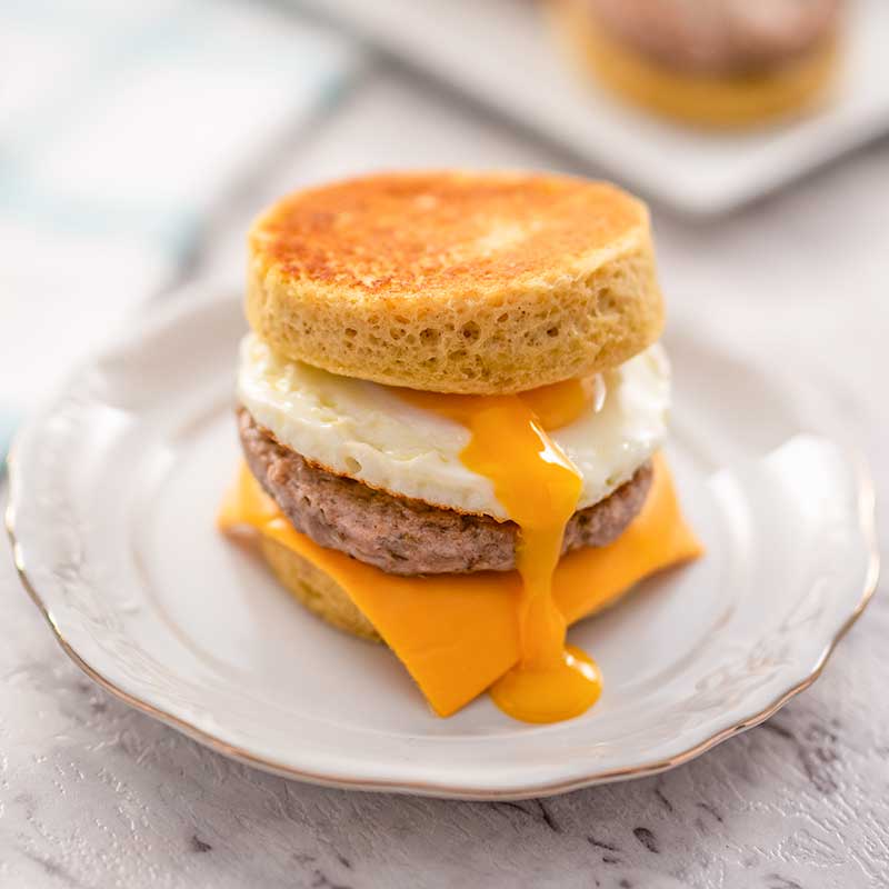Image of a keto sausage and egg muffin with egg yolk dripping down the front, it is sitting on a white plate