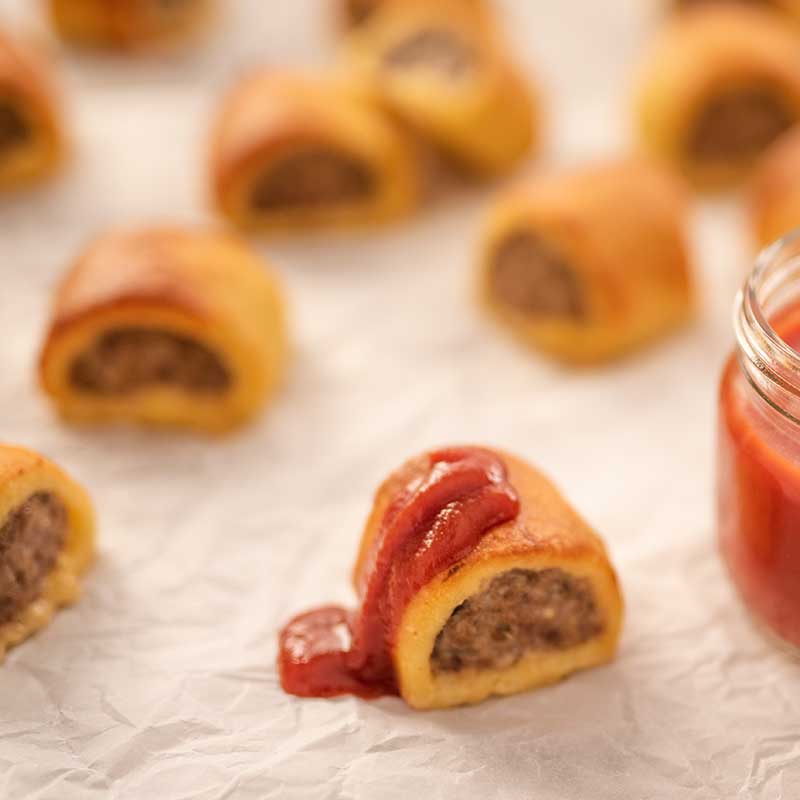 Image of bite sized keto sausage rolls one is drizzled with tomato ketchup