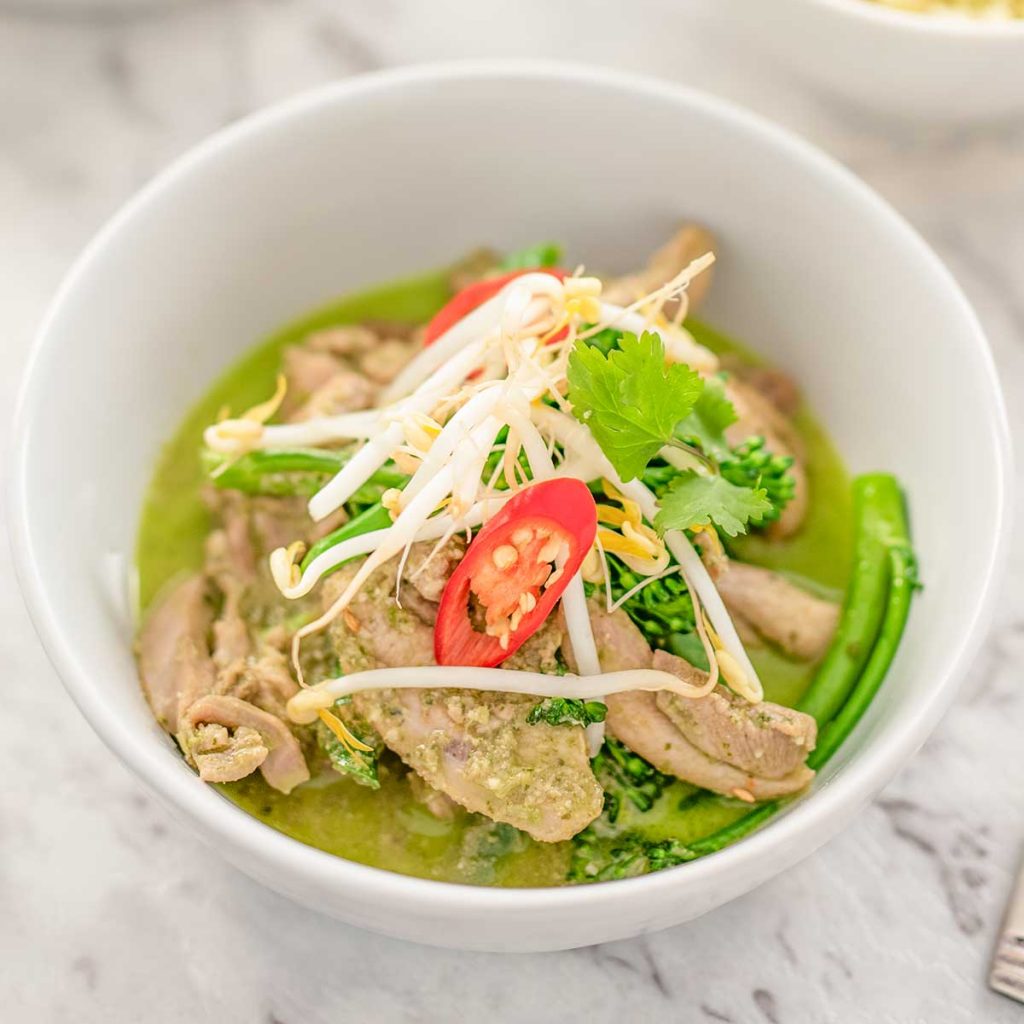 Image shows keto thai chicken green curry in a white bowl topped with bean sprouts, cilantro and a slice of red pepper