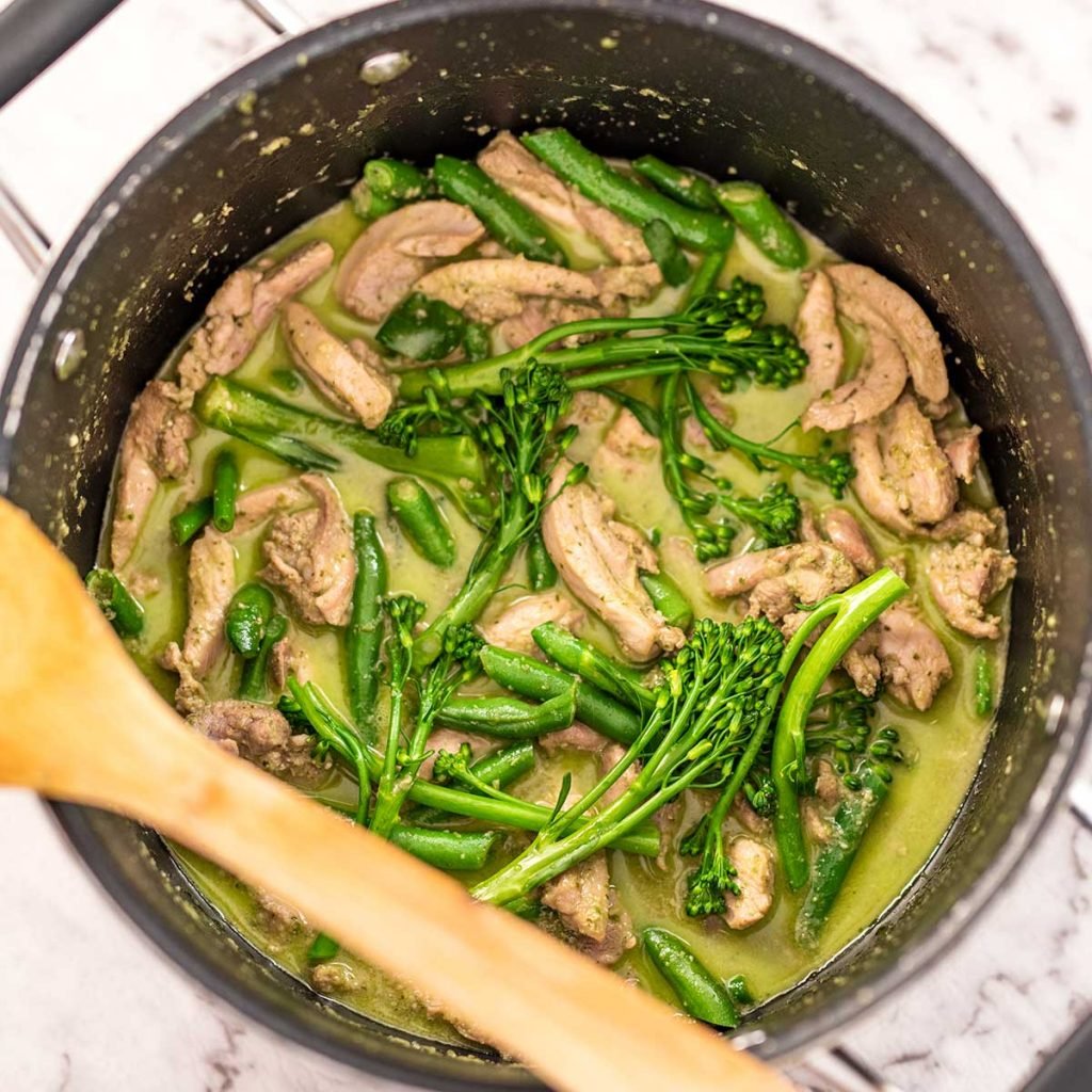 Image show a overhead view of keto thai green chicken curry in a black saucepan