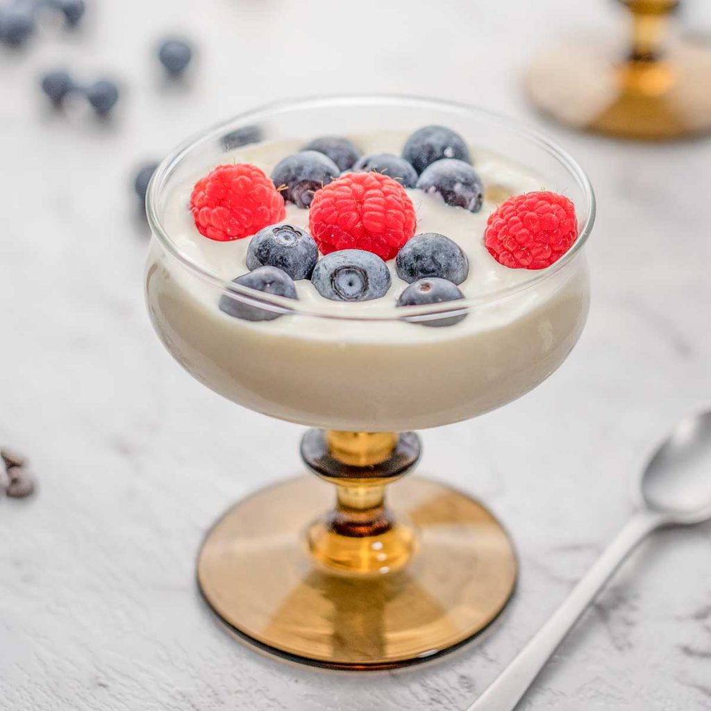 Glass filled with keto vanilla frozen yogurt and topped with blueberries and raspberries