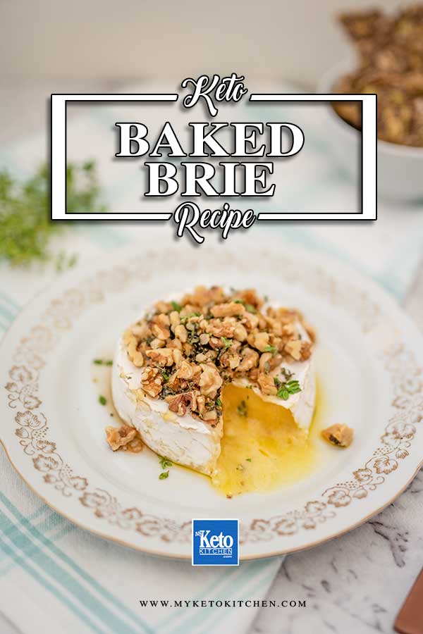 Image of a wheel of brie cheese on a white plate with gold edging, topped with walnuts, thyme and sugar free maple syrup. There is a slice removed and cheese is oozing out. There are crackers and a bunch of thyme in the background.