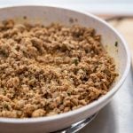Keto Italian Sausage sauteing in a speckled white frying pan