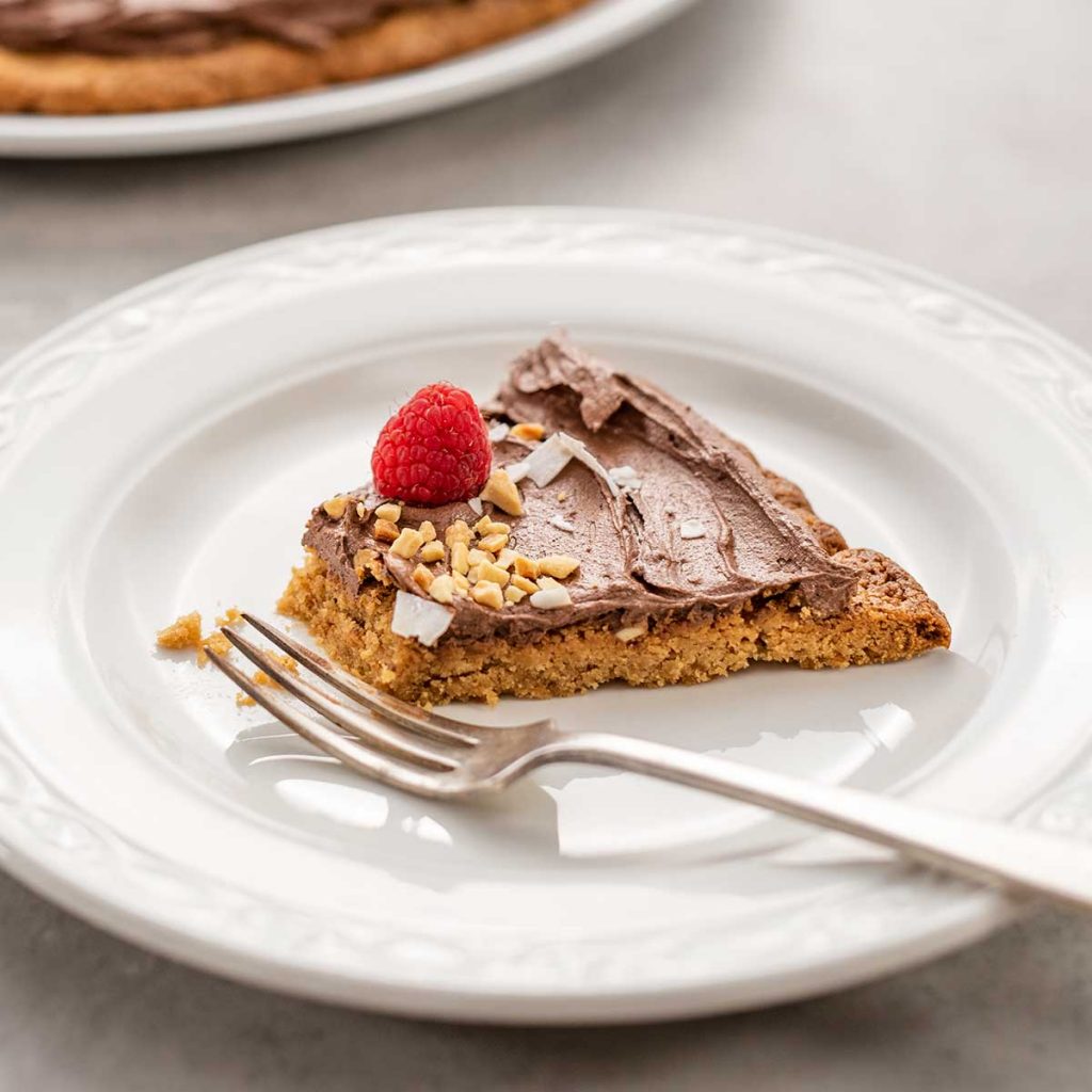 A slice of Keto Chocolate Peanut Butter Cookie Pizza with a bite missing on a white plate with a fork