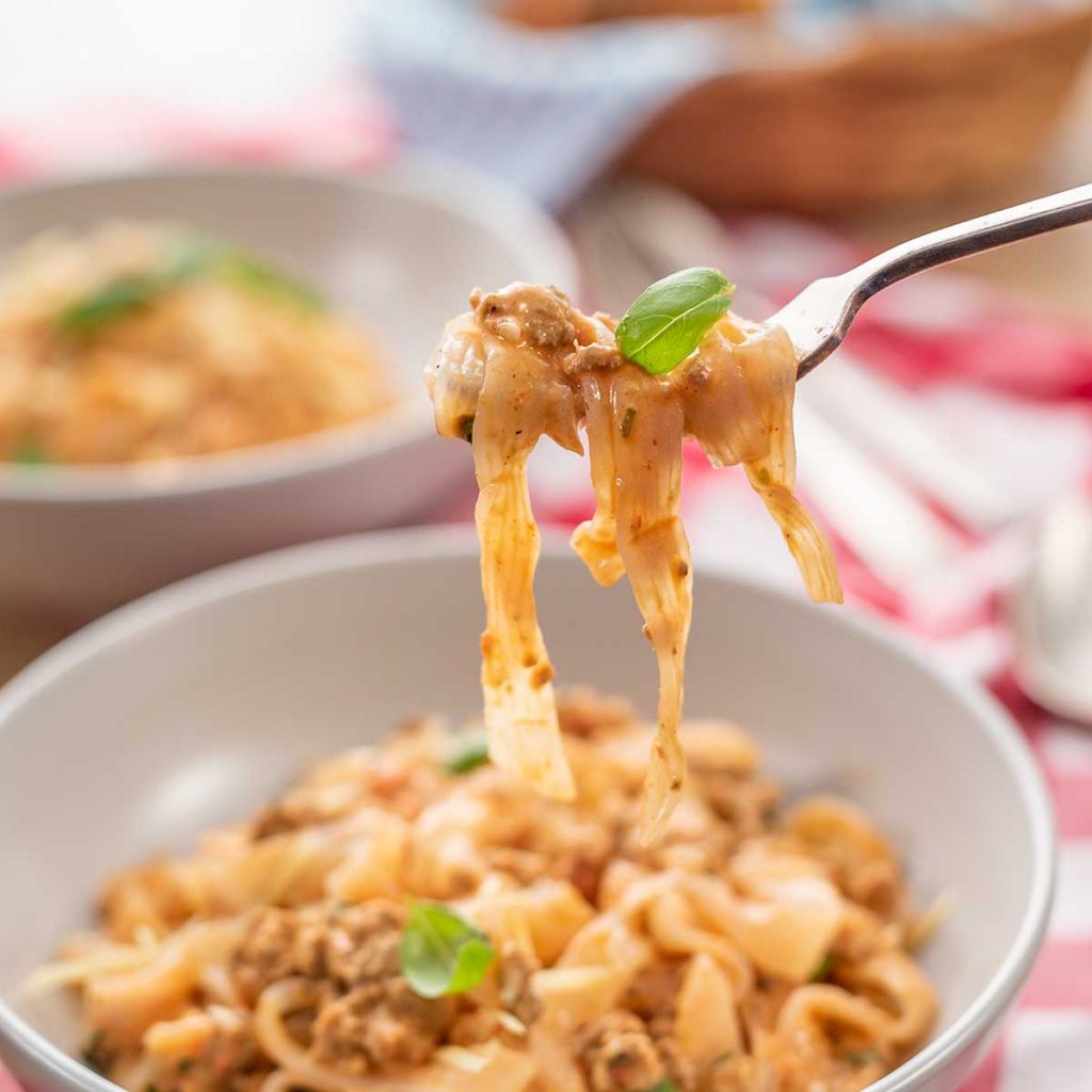 Keto Creamy Sausage Pasta in a grey bowl with a fork-ful being removed on red checkered cloth