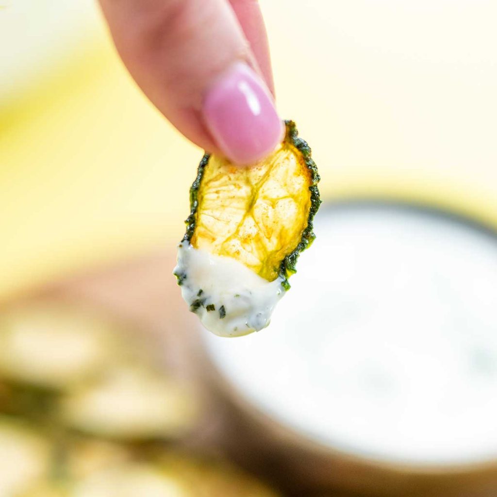 A Cucumber Chip with creamy dip on the end being held to the camera