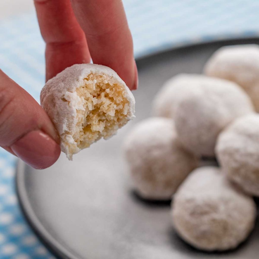 A Keto Snowball with a bite taken our being held to the camera, more snowball cookies are in the background