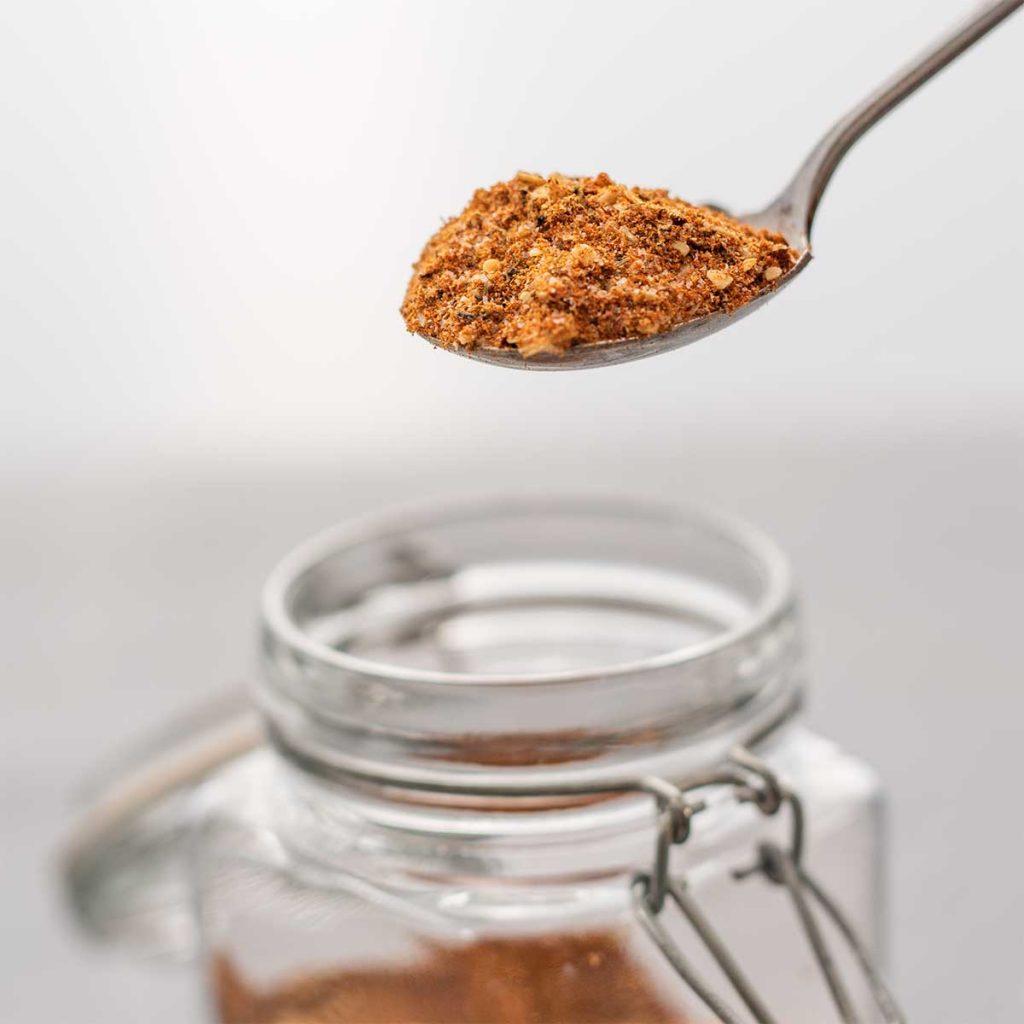 Montreal steak seasoning on a spoon being lifted from a glass jar