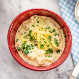 Keto Cheesy Grits in a red bowl, topped with cheddar cheese and chopped parsley