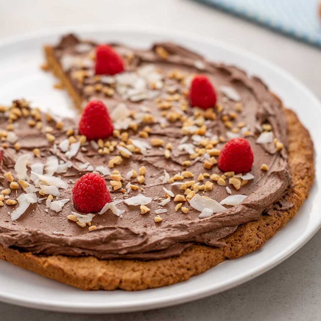 Keto Chocolate Peanut Butter Cookie Pizza with a slice missing on a white plate