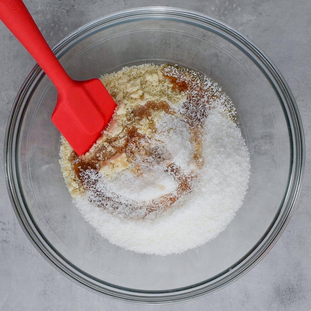 Keto Snowball Cookies ingredients in a mixing bowl with a red spatula