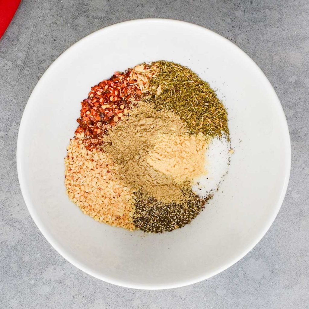 Montreal steak seasoning ingredients in a white bowl on a grey table