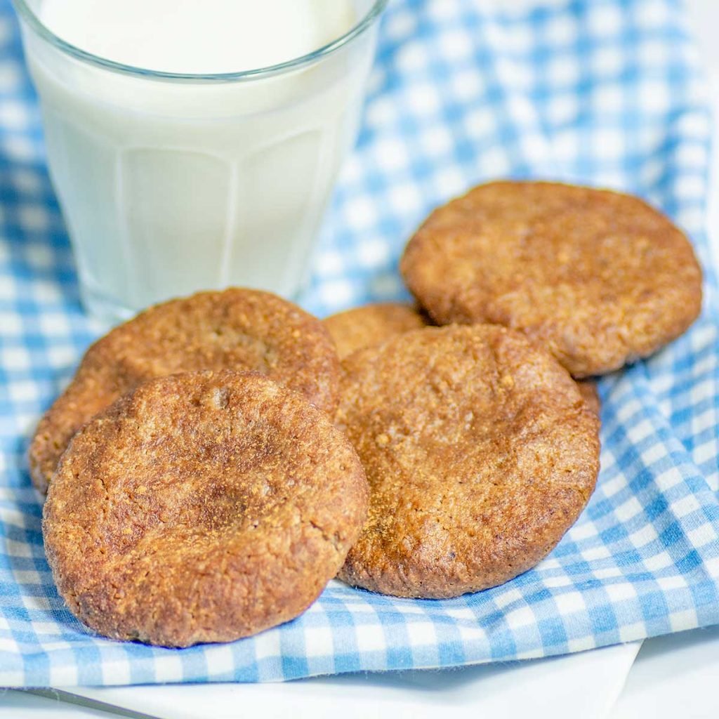 Keto Cinnamon Walnut Butter Cookies on a blue checked napkin with a glass of milk