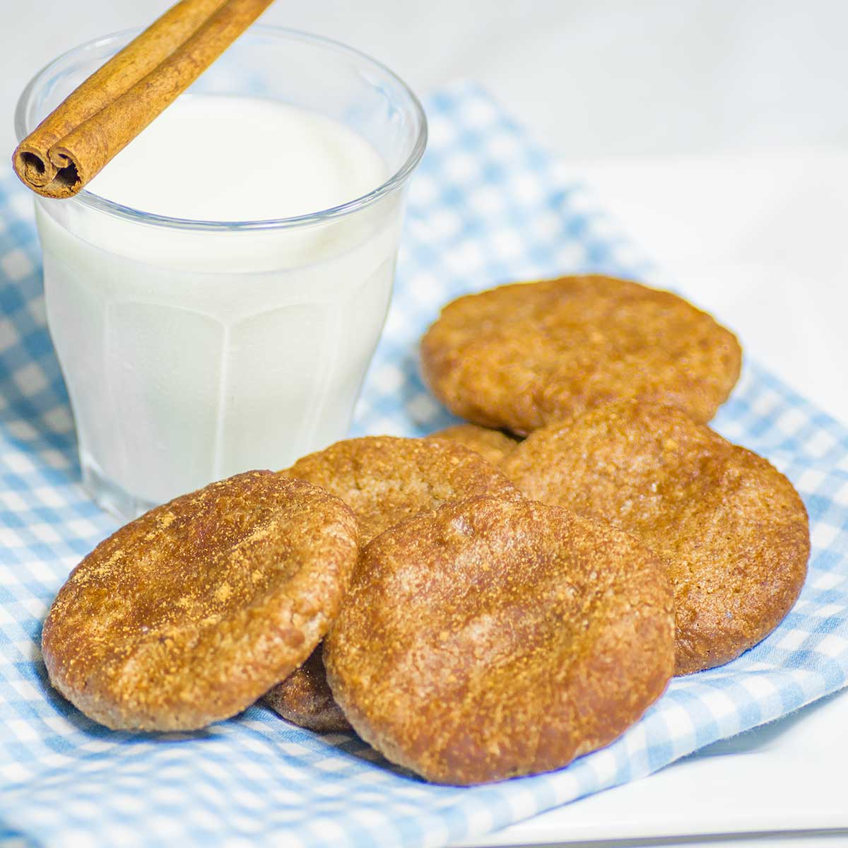 Keto Cinnamon Walnut Butter Cookies on a blue checked napkin with a glass of milk