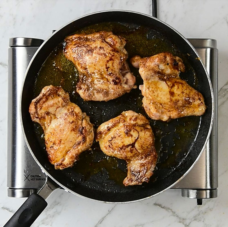 Cajun chicken thighs frying in a frying pan
