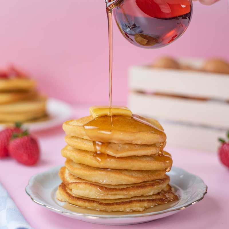 A stack of Keto Almond Flour Pancakes topped with butter and being drizzled with sugar-free maple syrup