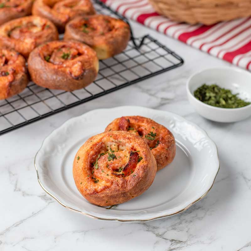Keto Pizza Scrolls on a white plate with a tray full behind