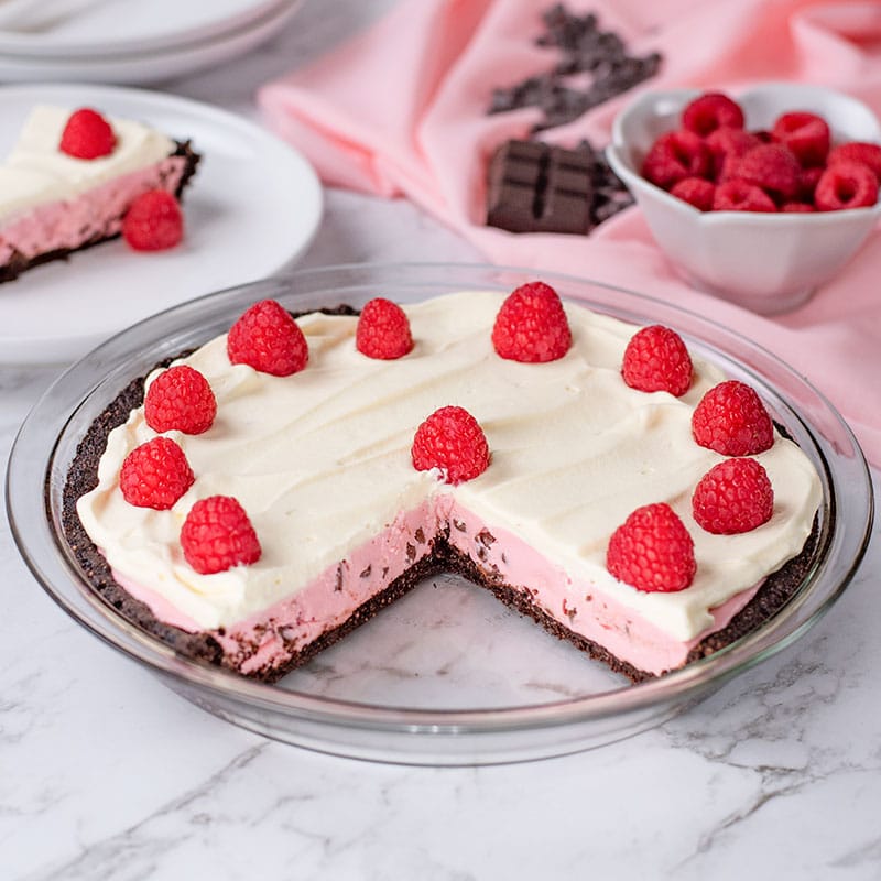 Keto Raspberry Cream Pie in a glass pie dish with a slice missing