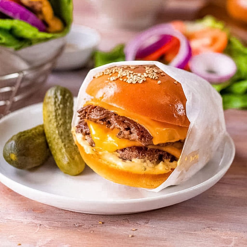 Keto cheeseburger on a plate with pickles.