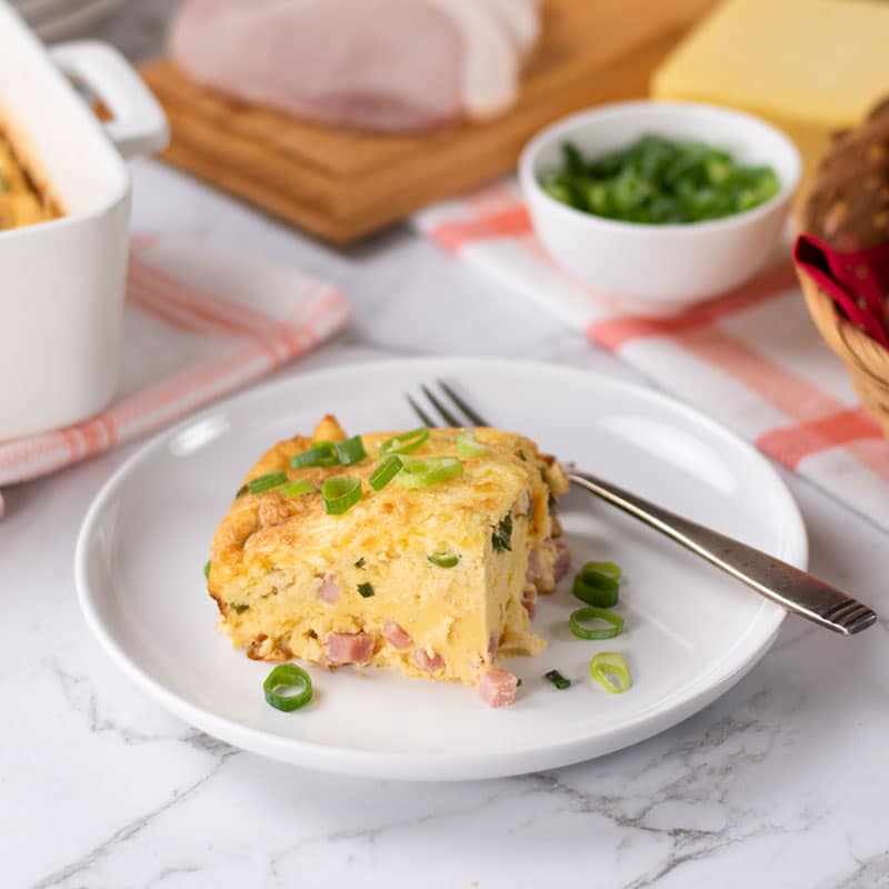 A slice of Keto Egg and Cream Cheese Bake on a white plate topped with scallions.