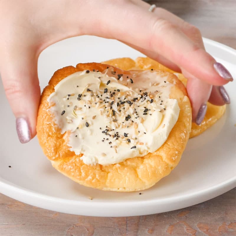 a slice of Keto Egg Bread topped with Cream Cheese and Everything Bagel Seasoning being picked up from a plate.