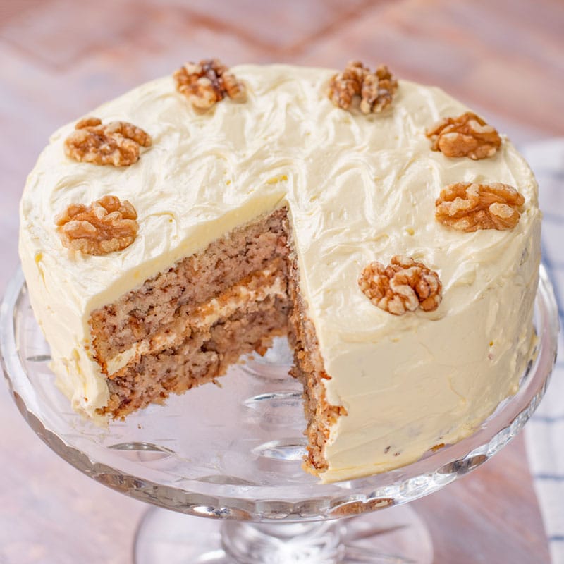 Keto Walnut Cake on a glass cake stand with a slice removed.