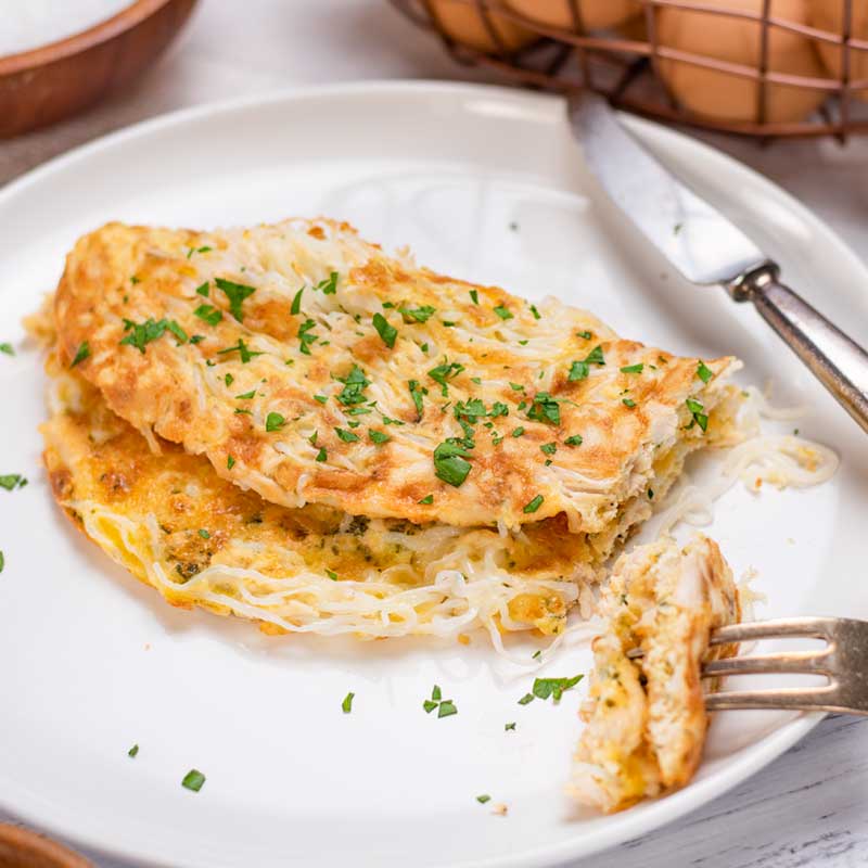 A Keto Chicken Noodle Omelette on a white plate with a slice cut from one end.