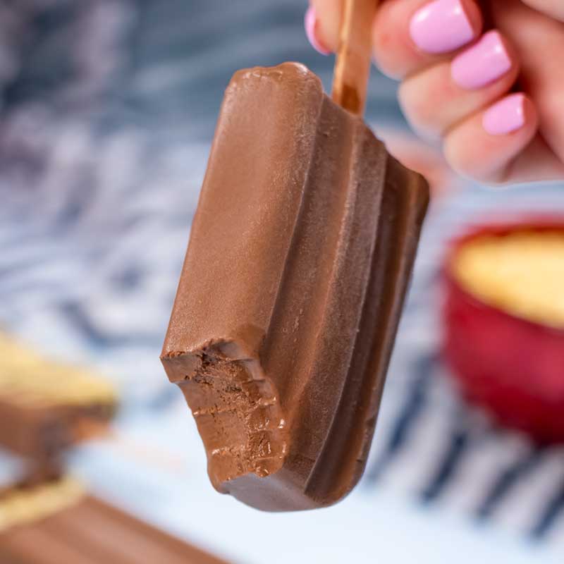 A Keto Chocolate Ice Cream Bar with a bite taken out being held up to the camera.