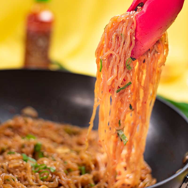 Keto Spicy Noodles being lifted from the wok with tongs.