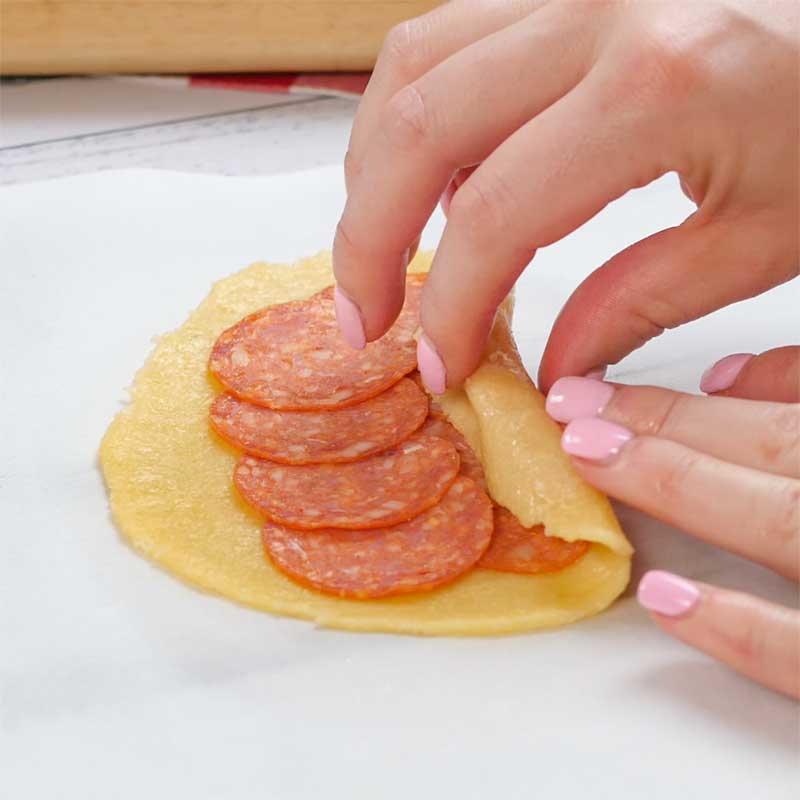 Dough filled with pepperoni being rolled up into a pepperoni roll.