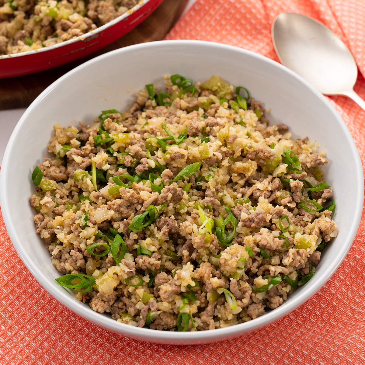 Keto dirty rice in a white bowl on a red table cloth.