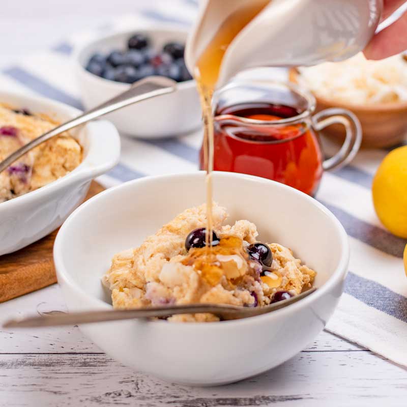 Keto Blueberry Baked Oatmeal in a bowl being covered in sugar-free maple syrup.