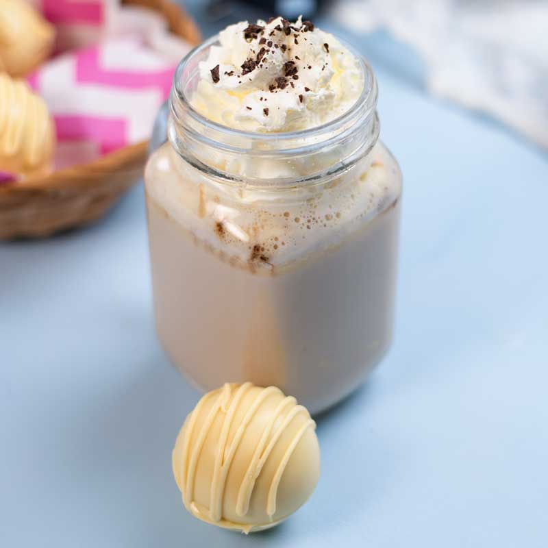 A Keto White Chocolate Coffee Bomb in front of a glass of white chocolate coffee.