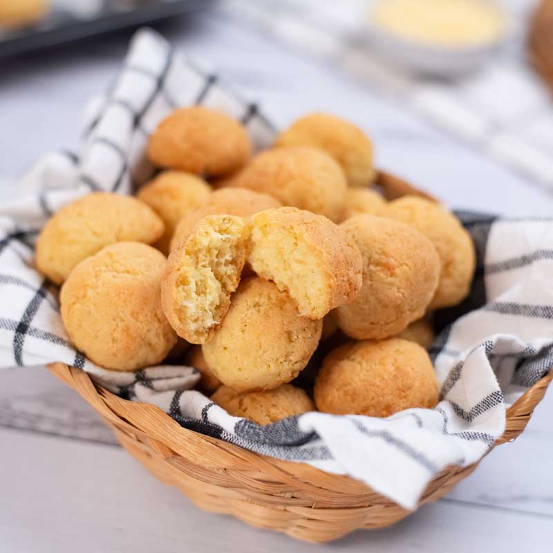 Keto Brazilian Cheese Bread in a basket, with one bun torn in half to show the fluffy insides.