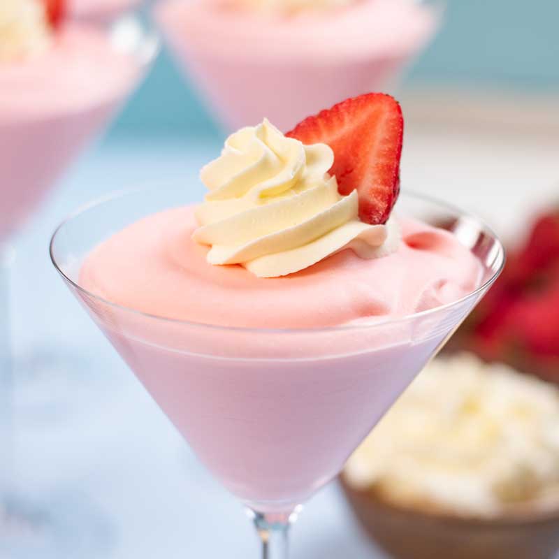Keto strawberry mousse in a martini glass topped with whipped cream and a slice of strawberry.