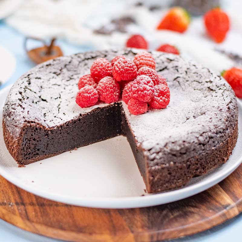 Keto Flourless Cake topped with raspberries with a slice removed to show the inside.