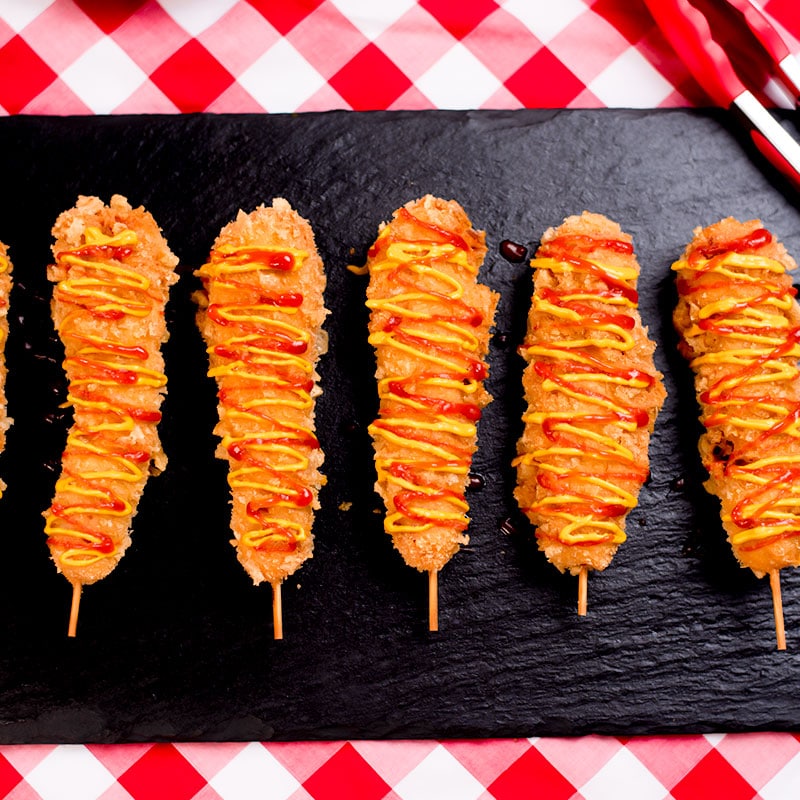 Keto corn dogs on a black slate tray.